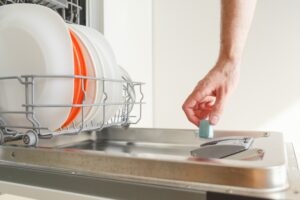 Man puts a chemical dishwasher tablet into the dishwasher machine