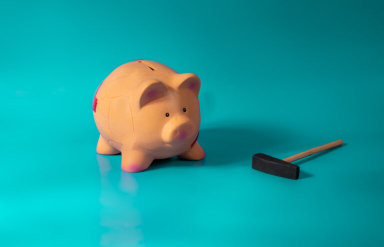 Sad piggy bank, next to a hammer, against a light blue background.